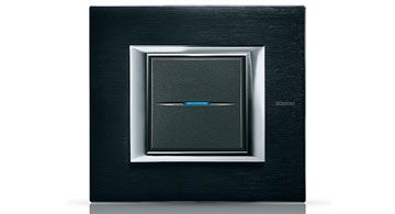 Ein moderner Lichtschalter von Legrand in schwarzem Design mit silbernem Rahmen und blauem LED-Streifen in der Mitte.